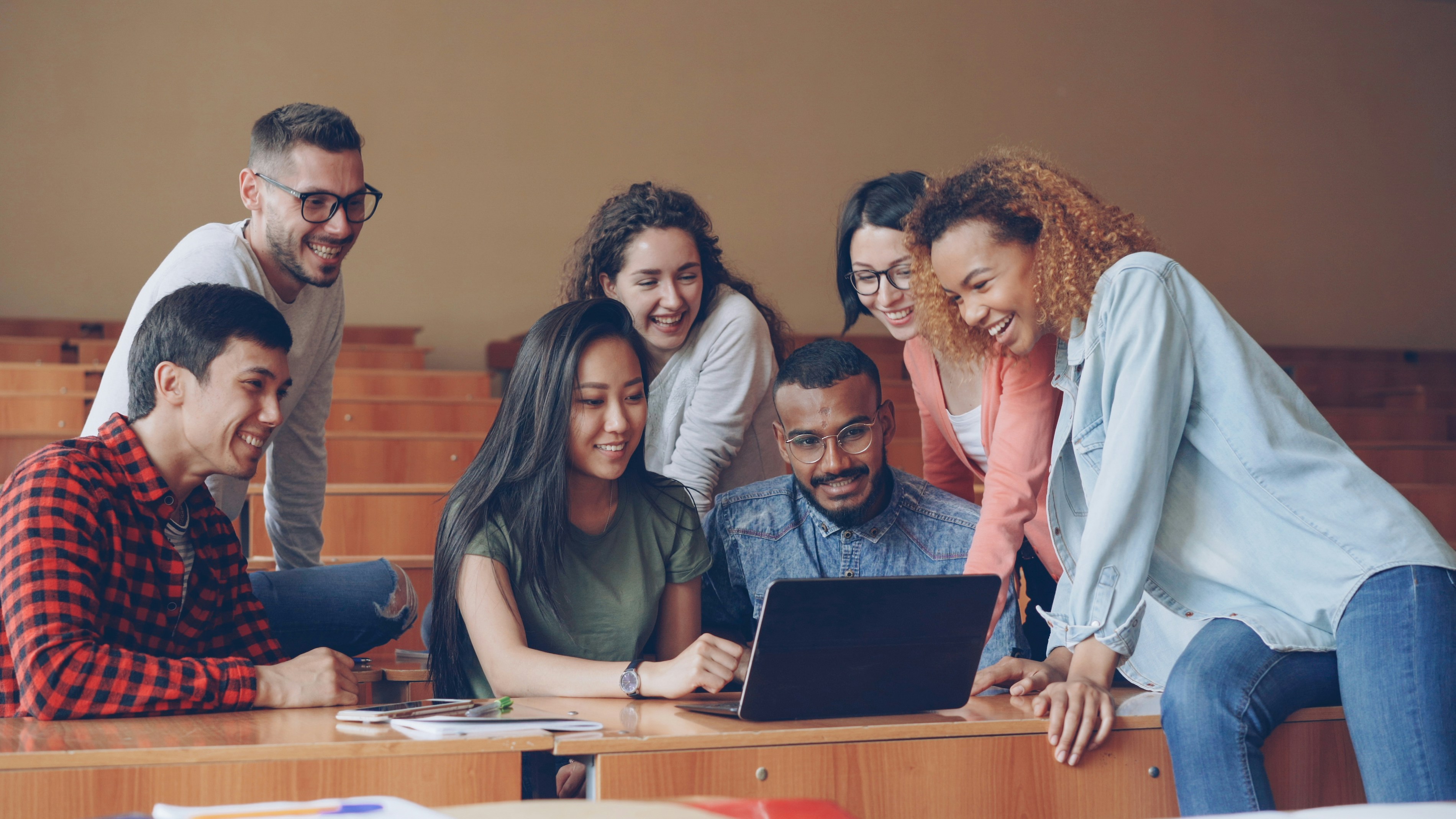 Students gathered around a laptop in a lecture hall.